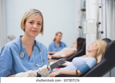 Nurse Holding A Clipboard Next To A Transfused Patient In Hospital Ward