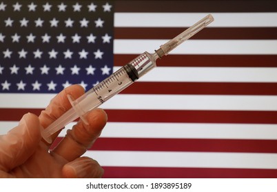 Nurse Holding Syringe With United States Flag In The Background. Covid-19 Vaccine In The USA Concept.