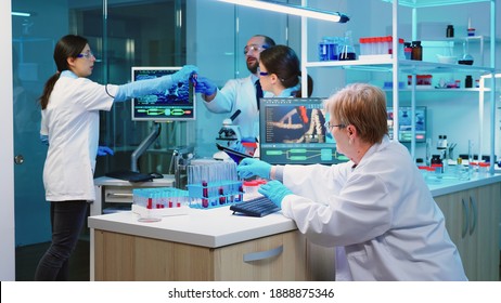 Nurse Holding Tablet Computer With Scientific Informations While Chemist Using Microscope With Chemical Test Tube Near, In Lab Background At Night. Medical Science Research And Development Concept