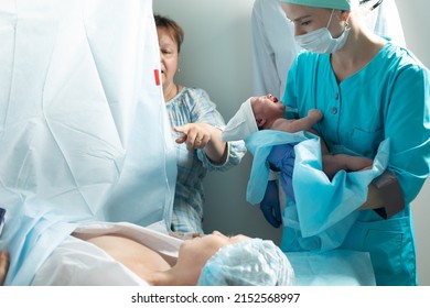 Nurse holds newborn baby close to mother in hospital