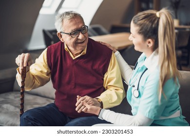 Nurse home caregiver is assisting old man at his home. Professional health support for elderly people.