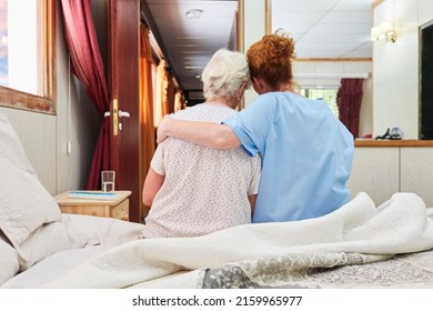 Nurse Hugs Elderly Woman Sitting On Bed In Hospice For Comfort