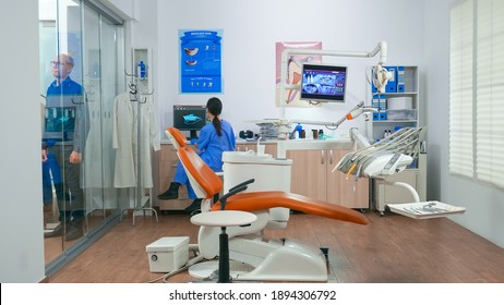 Nurse inviting next patient in stomatology room showing to lie on chair. Dentistry assistant sitting in consultation dental room with elderly woman while doctor speaking with old man in background.