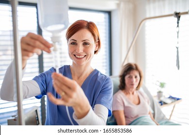 A Nurse With IV Drip And Patient In Bed In Hospital Room.