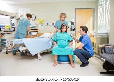 Nurse And Man Consoling Pregnant Woman Sitting On Fitness Ball In Hospital