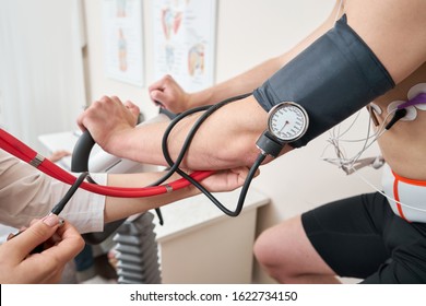 The nurse measures arterial tension. Man patient, pedaling on a bicycle ergometer stress test system for the function of heart checked. Athlete does a cardiac stress test in a medical study