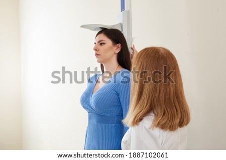 Nurse measures the height of young woman at the doctor office