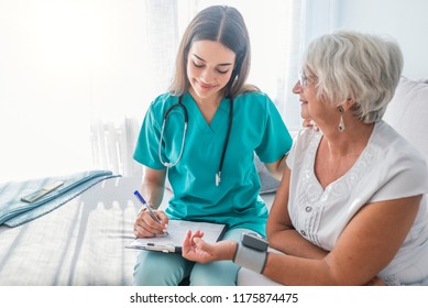 Nurse measuring blood pressure of senior woman at home. Smiling to each other. Young nurse measuring blood pressure of elderly woman at home. Doctor checking elderly woman's blood pressure