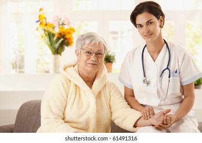 Nurse measuring pulse rate of senior woman at home. Looking at camera, smiling.?