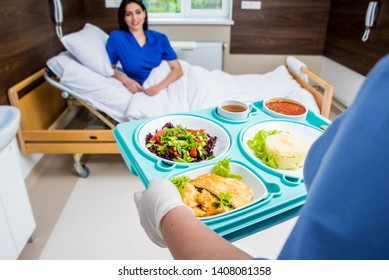 Nurse in medical coat is holding a tray with breakfast for the young female patient. Hospital food concept - Powered by Shutterstock