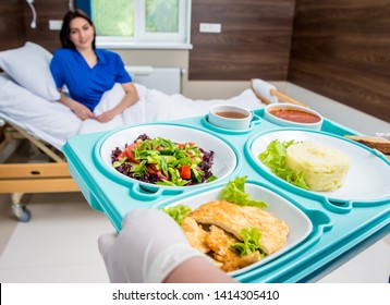 Nurse in medical coat is holding a tray with breakfast for the young female patient. Hospital food concept - Powered by Shutterstock