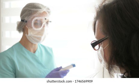 Nurse in a medical mask, glasses and gloves measures the patient's temperature with a non-contact infrared thermometer.