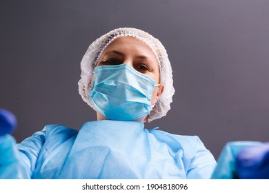 A Nurse In A Medical Suit And A Mask Makes A Selfie On A Gray Background.