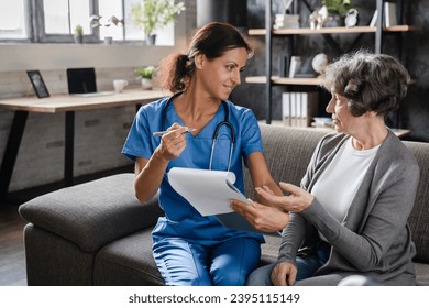 Nurse medical worker doctor caregiver taking notes of medical insurance, prescribing pills medications, diagnosing elderly senior woman patient at home hospice - Shutterstock ID 2395115149