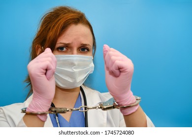 A Nurse On A Blue Background Shows Hands In Handcuffs, Closeup. Doctor Arrested For A Bribe From A Patient, Concept