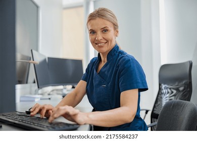 Nurse On Duty Working On Computer At The Reception Desk In Modern Clinic. High Quality Photo