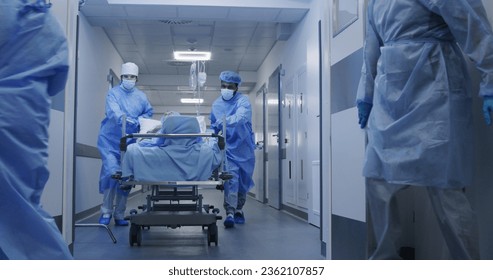 Nurse and paramedic open medical facility corridor doors. Multi ethnic surgeons push stretcher with lying elderly patient to operating room. Medical personnel work in emergency department. Slow motion - Powered by Shutterstock