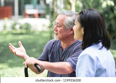 Nurse With Patient Sitting On Bench Together Talking. Asian Old Man And Young Woman Sitting Together Talking. Relax Mood.