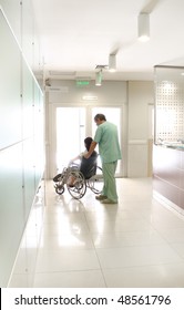 Nurse And A Patient Using A Wheelchair At A Hospital Hall