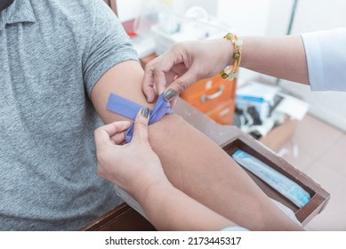 A nurse or phlebotomist tying a rubber IV Tourniquet placed above the elbow. Venipuncture for blood testing or hematology analysis.