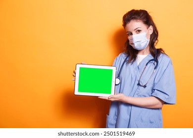 Nurse practitioner with face mask horizontally holding tablet with green screen. Female healthcare specialist grasping digital device displaying isolated copyspace mockup template. - Powered by Shutterstock