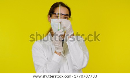 Nurse in protective medical mask, glasses, latex gloves and test tube in hands. Girl in a white coat on a yellow background