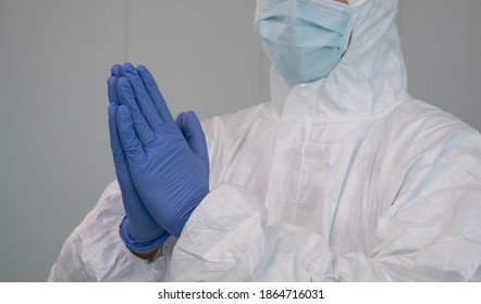 A Nurse In A Protective Suit PPE Praying During The Pandemic Caused By Covid-19. Put Your Gloved Hands Together To Pray.