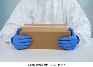 A Nurse In A Protective Suit Shows A Box With Both Hands In A Hospital. The Healthcare Worker Receives Medical Supplies To Fight Coronavirus Covid 19. Doctor Wearing A PPE And Gloves