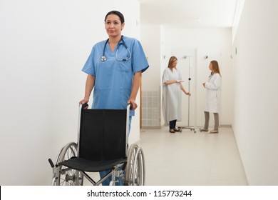 Nurse pushing empty wheelchair with doctor and patient talking in hospital corridor, Healthcare workers in the Coronavirus Covid19 pandemic - Powered by Shutterstock