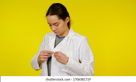 Nurse Puts On A White Coat On A Yellow Background. Young Girl Doctor Getting Ready For Work