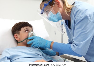 Nurse Puts Oxygen Mask On Patient Child In Hospital Bed, Wearing Protective Visor Mask, Corona Virus Covid 19 Protection Concept, 