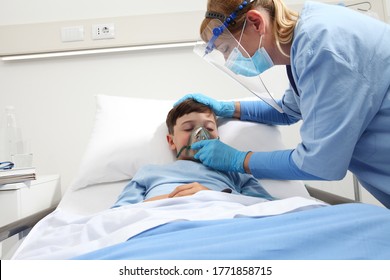 Nurse Puts Oxygen Mask On Patient Child In Hospital Bed, Wearing Protective Visor Mask, Corona Virus Covid 19 Protection Concept, 