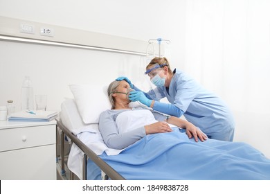 nurse puts oxygen mask on elderly woman patient lying in the hospital room bed, wearing protective gloves and visor medical mask, coronavirus covid 19 protection concept - Powered by Shutterstock