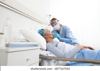 Die Krankenschwester stellt eine Sauerstoffmaske auf ältere Patientinnen, die im Krankenhausschlafzimmer liegen, und trägt Schutzhandschuhe und ärztliche Schutzmaske, das Schutzkonzept Coronavirus covid 19