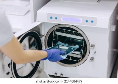 The Nurse Is Putting The Dental Equipment To The Cleaning Machine. She Is Wearing Blue Medical Gloves. The Equipment Is In The Silver Plate And Blue Packet.