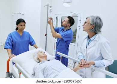 Nurse putting drip on elderly patient lying on gurney while being examined by experienced woman doctor. Medical assistants will take injured woman to her medical ward - Powered by Shutterstock