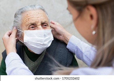 Nurse putting on surgical mask on elderly ill woman - coronavirus protective protocol