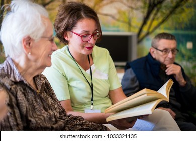 Nurse Reading Book To Elderly Group Of People