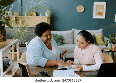 Nurse in rose scrubs familiarizing African American female patient with form in calm atmosphere - Powered by Shutterstock