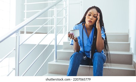 Nurse In Scrubs Takes Coffee Break In Busy Hospital. Female Nurse Sitting On The Floor And Looking Distraught. Shot Of A Young Nurse Looking Stressed Out While Sitting At A Window In A Hospital