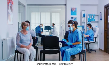 Nurse and senior patient going in hospital examination room from waiting area. Doctor inviting old woman for consultation in office. Wearing mask against coronavirus. - Shutterstock ID 1804803289