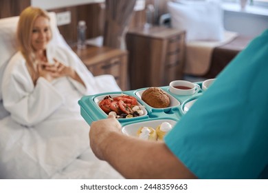 Nurse serving dietary meal to inpatient in medical facility ward - Powered by Shutterstock