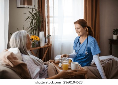 Nurse serving food in the bed to a lying patient at her home. - Powered by Shutterstock