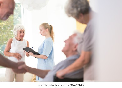 Nurse Sharing Health Information With Senior Patient While Standing In Common Room