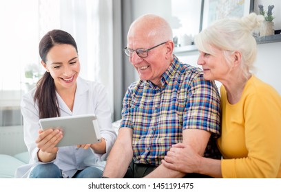 Nurse showing medical raport using tablet to senior couple at home