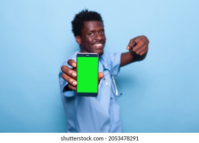 Nurse Showing Smartphone With Vertical Green Screen. Medical Assistant Holding Device With Chroma Key And Mockup Template For Isolated Background On Display. Man With Modern Phone