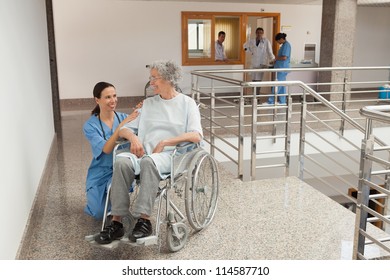 Nurse Smiling And Kneeling Beside Old Women Sitting In Wheelchair. Healthcare Workers In The Coronavirus Covid19 Pandemic