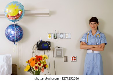 Nurse Standing Beside Get Well Balloons In Hospital Ward At Camera