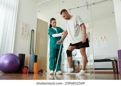 Nurse supporting patient learning to step on hurt leg leaning on crutch - Powered by Shutterstock