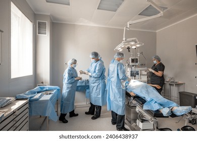 Nurse with surgeon preparing for an operation, wearing sterile uniform in operating room with a patient lying. Concept of sterility during surgical treatment - Powered by Shutterstock